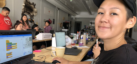 Youth smiling in camera while sitting in front of a laptop at the FabLab Onaki